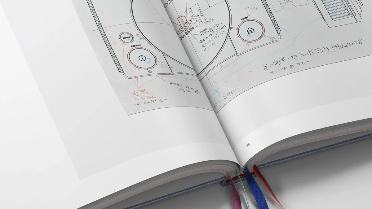 Original hand-annotated engineering blueprints from Sony's hardware archives alongside the four colored PlayStation symbol ribbon bookmarks.