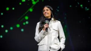 Xbox CEO Asha Sharma holding an Xbox microphone on stage during a Microsoft presentation