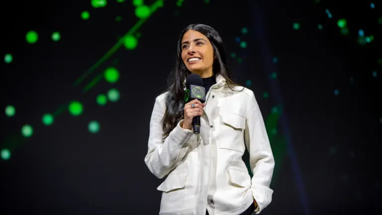 Xbox CEO Asha Sharma holding an Xbox microphone on stage during a Microsoft presentation